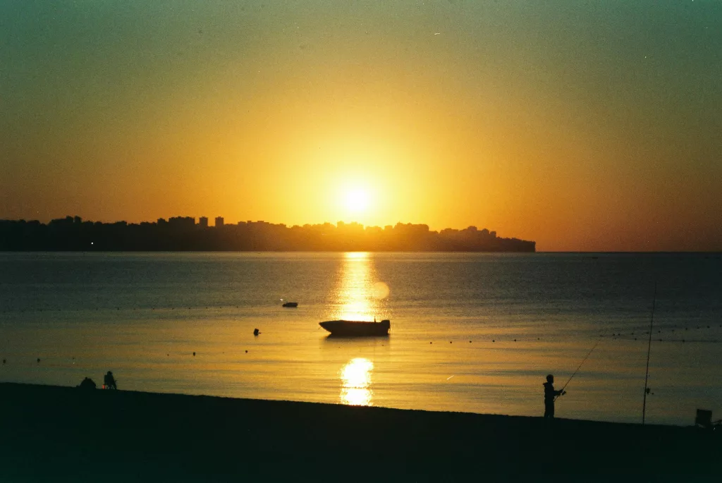 Serene ocean view at sunset with a lone fishing silhouette and a boat.